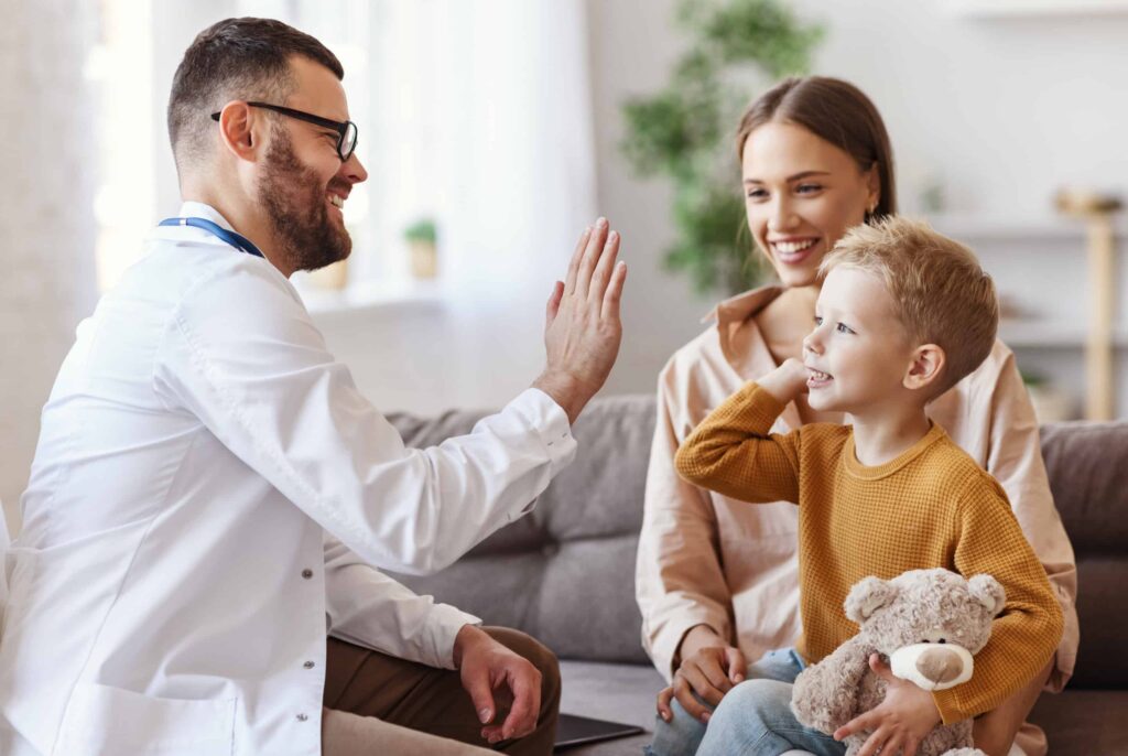 family doctor pediatrician conducts examination of child boy who came with his mother,  and giving high five to him