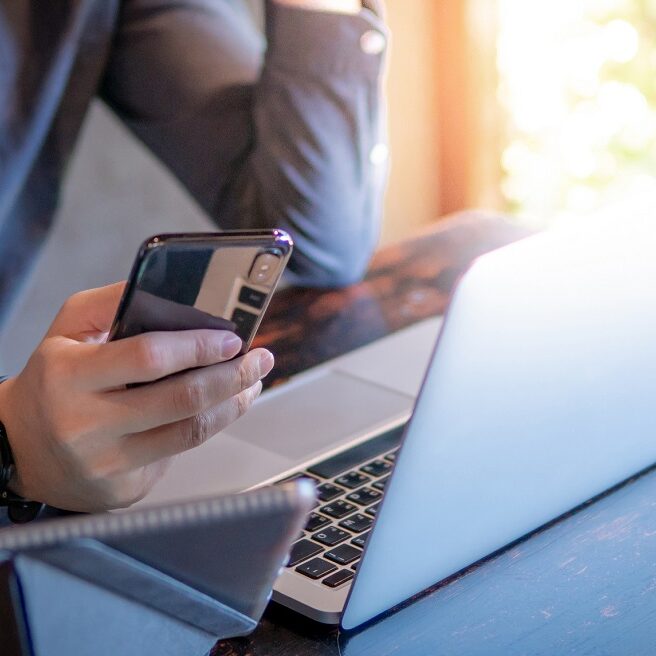 Male hand holding smartphone. Businessman using laptop computer and digital tablet while working in the cafe. Mobile app or internet of things concepts. Modern lifestyle in digital age.