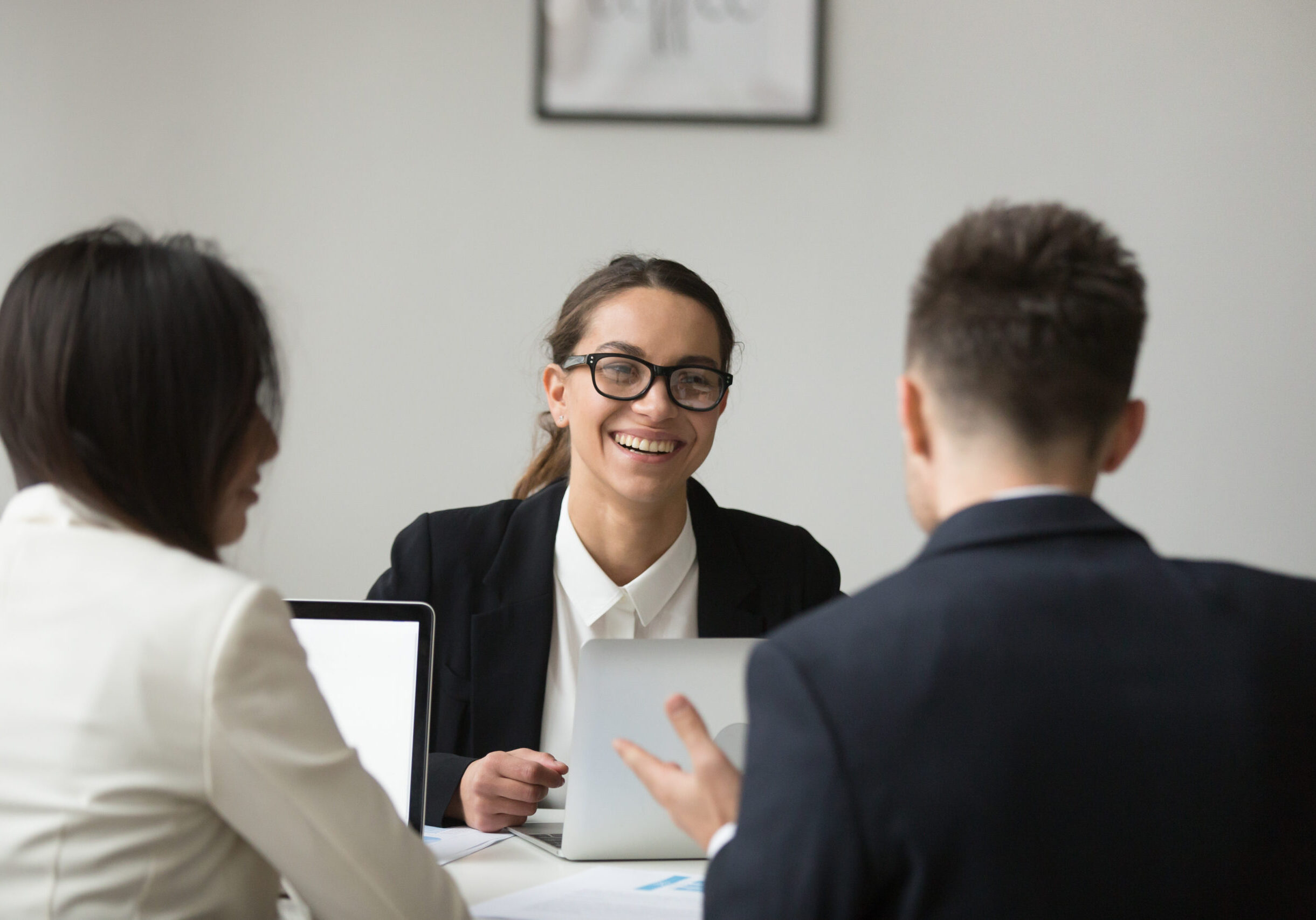 Smiling female CEO wearing glasses talking with company subordinates, discussing business strategies. Colleagues negotiating in positive atmosphere, working at laptops. Cooperation, leadership concept