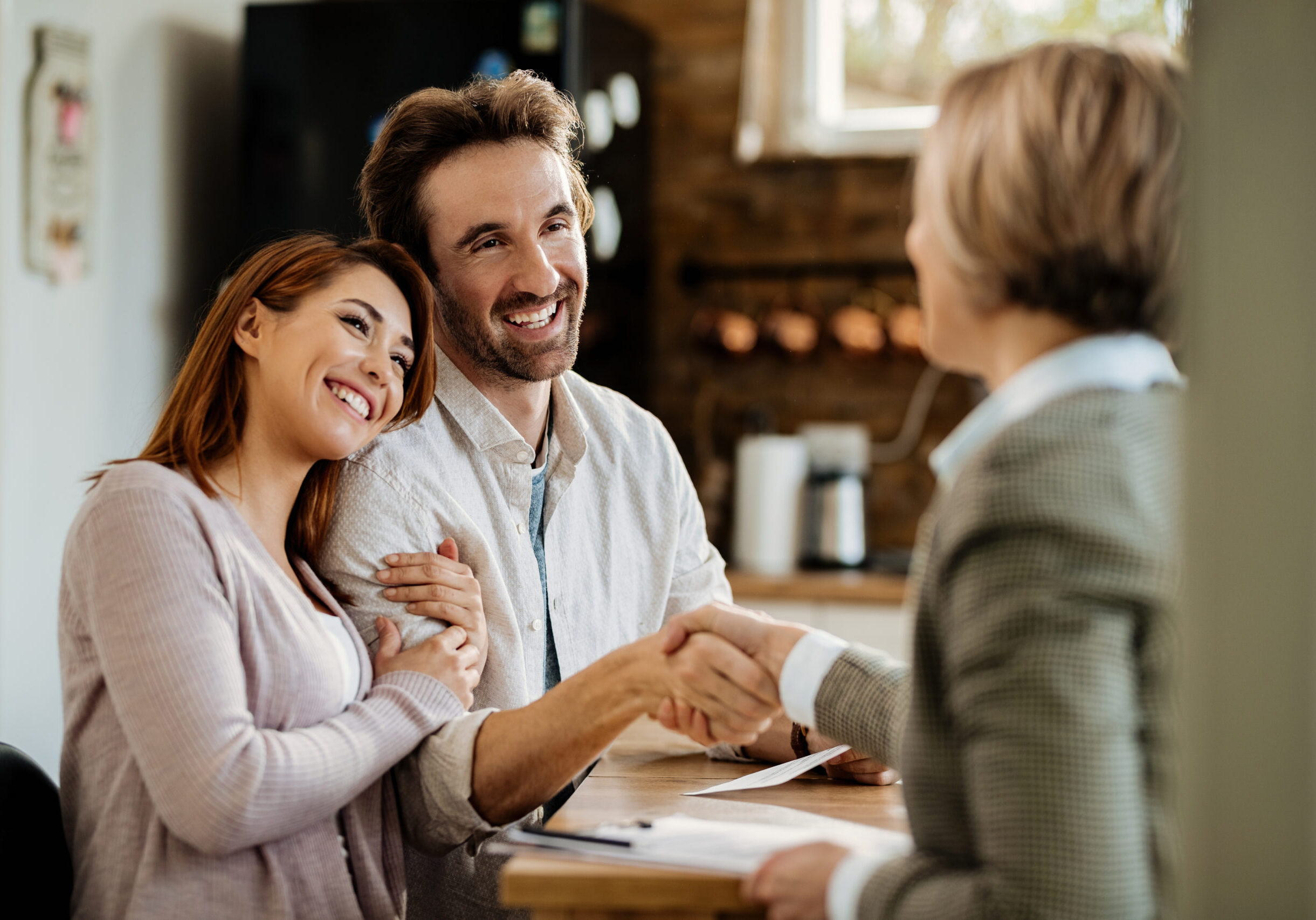 Young happy couple came to an agreement with their insurance agent. Focus is on man shaking hands with the agent.