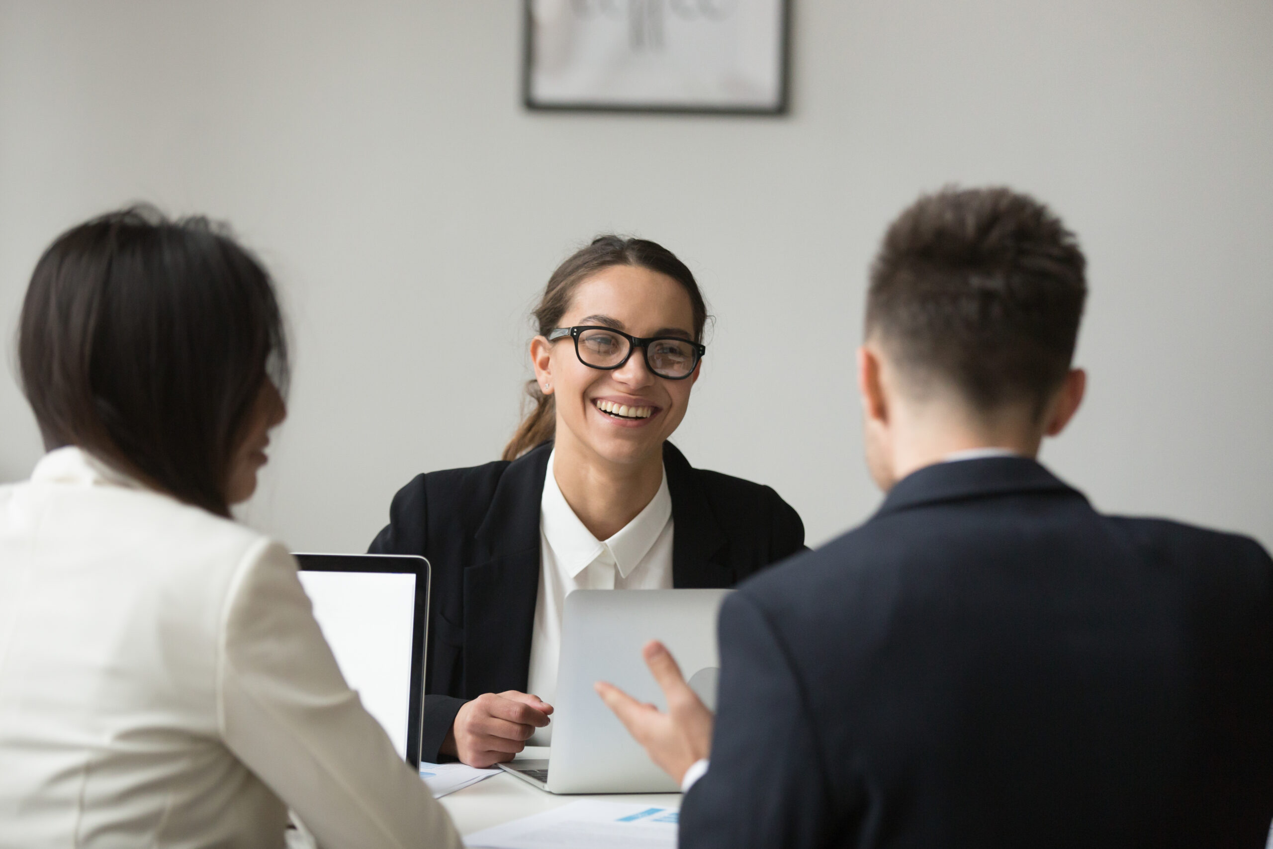Smiling female CEO wearing glasses talking with company subordinates, discussing business strategies. Colleagues negotiating in positive atmosphere, working at laptops. Cooperation, leadership concept